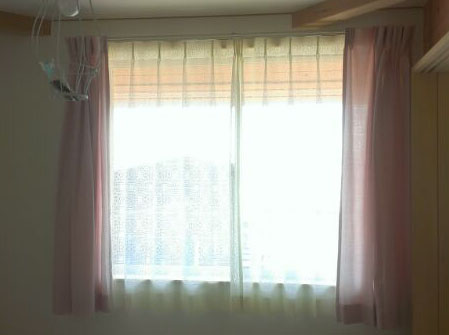 ピンク色の無地のカーテンと、お洒落な編みのレースカーテン